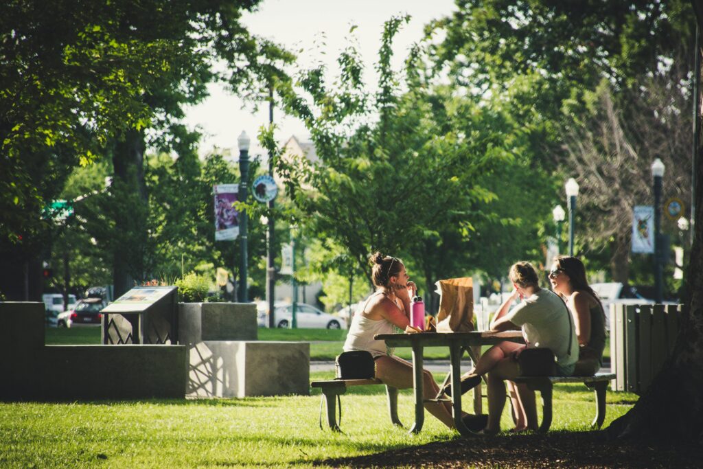 A group of friends sitting at a picnic table in a park, enjoying leisure time under sunny skies.