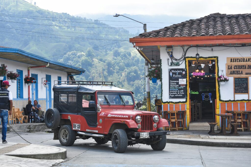 A classic red Jeep Wrangler is parked on a vibrant street in a Colombian town.