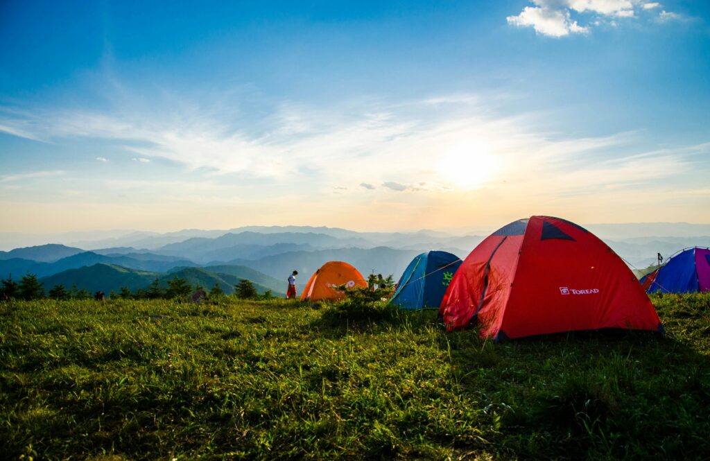 pexels-photo-1687845-1687845 Vibrant tents on a grassy mountain ridge with a stunning sunrise view, ideal for adventure.