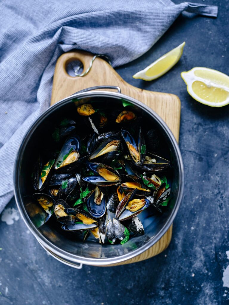 pexels-photo-30649002-30649002 Top view of a pot filled with steamed mussels, garnished with fresh herbs and served with lemon wedges.